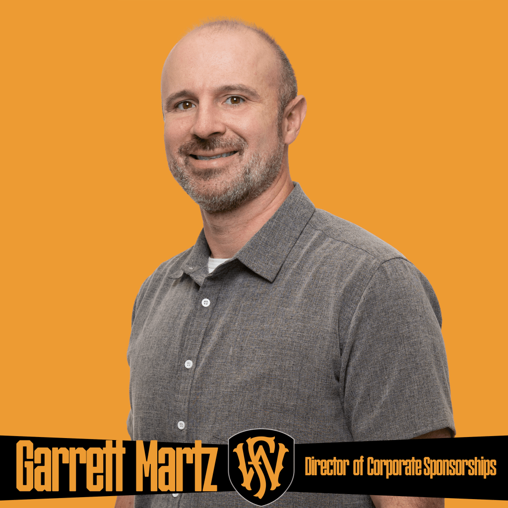 A smiling man wearing a gray button-down shirt stands in front of an orange background. The graphic features the Fort Wayne FC logo and text reading “Garrett Martz | Director of Corporate Sponsorships.” Promotional image showcasing Fort Wayne FC’s partnerships and corporate sponsorship leadership.